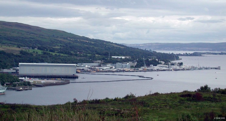 Over looking Faslane base from the North west side of Gareloch
This view gives an idea of the size of the ship lift building, the equivalent of 11 stories high.  The ship lift is the largest in Europe at 615 metres long and 25 metres wide it is capable of lifting 28,000 tones.  In the distance the river clyde can be seen with the town of Greenock on the opposite side of the river.
