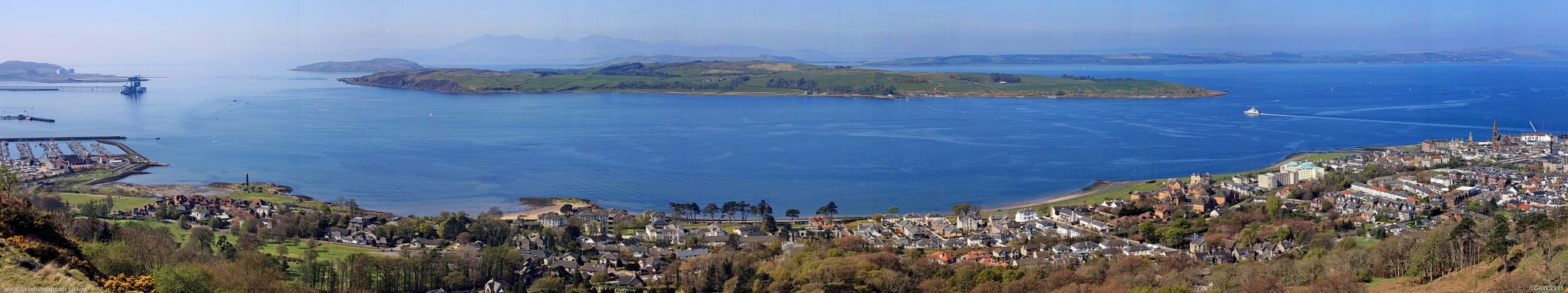 Panoramic view over looking the Great Cumbrae
Taken from Castle Hill above Largs, there's a footpath that leads from Douglas Park in the town to the top of this hill.  On the left is the Ore terminal at Hunterston, the Wee Cumbrae, the Great Cumbrae and in the distance behind the mountains of the Isle of Arran.  On the right behind the Cumrae is the Island of Bute.  The Car ferry can be seen making the short crossing over to the Great Cumbrae from Largs pier.
